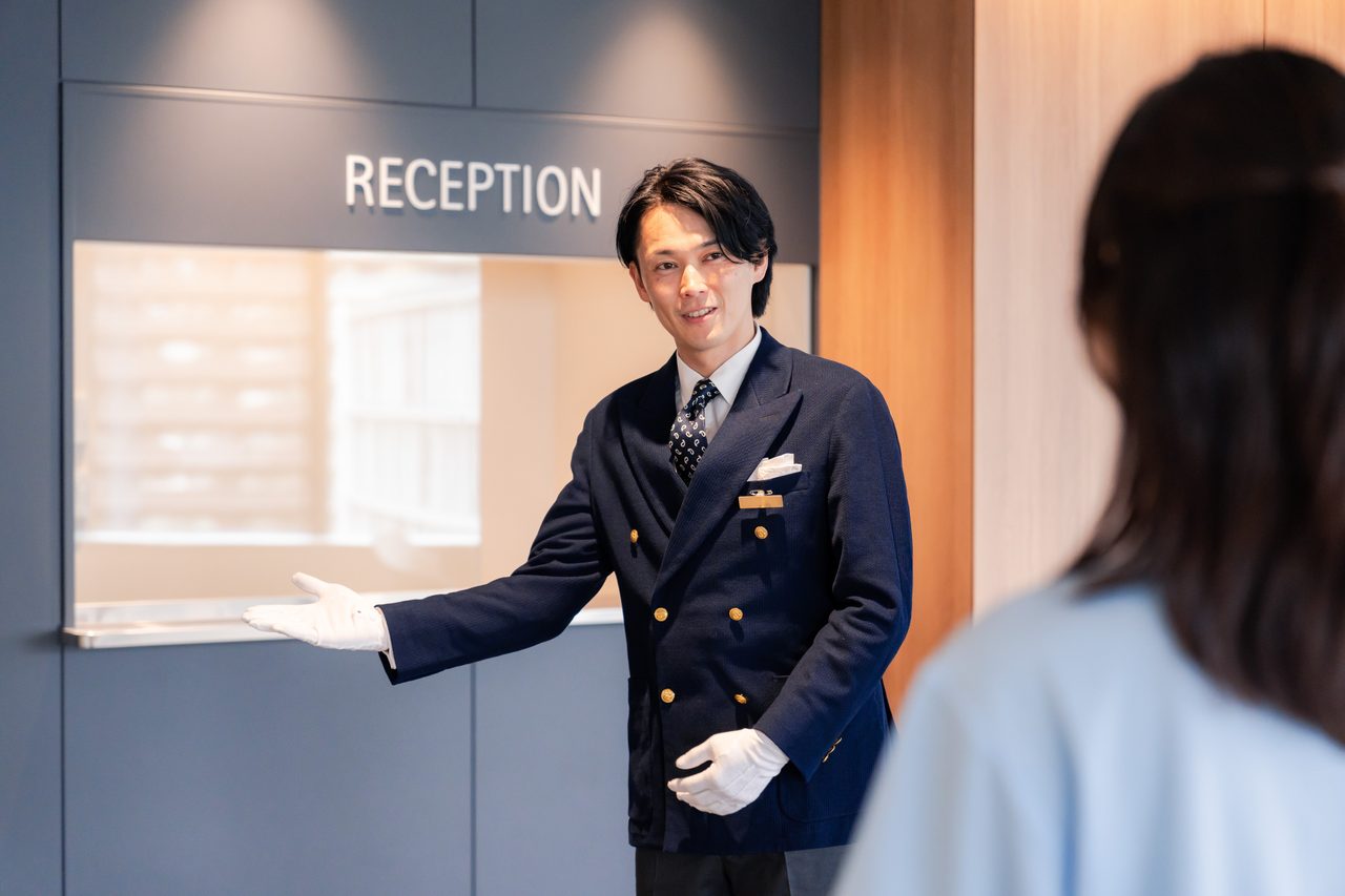 ホテルの受付でスタッフが来訪者を案内している様子（イメージ）